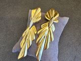 boucles d'oreilles en feuille d'or posées sur un coussin, sur fond gris