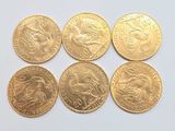 six pièces d'or de formes et de tailles différentes sur une surface blanche