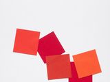 four squares of red and orange colored paper on a white surface