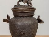a small metal pot with a bird on top of it