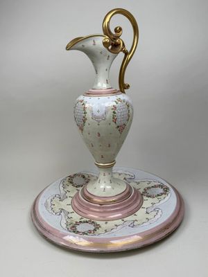un vase blanc et rose muni d'une anse dorée, posé sur une assiette