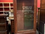 a tall wooden cabinet with a glass door in a room