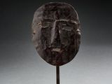 un masque en bronze posé sur un socle en bois, sur fond noir