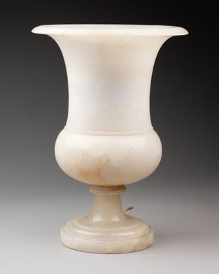 un vieux vase blanc posé sur une table près d'un mur gris