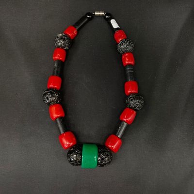 un collier rouge et noir orné d'une perle verte