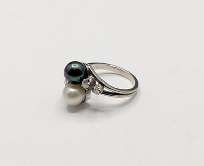 un gros plan d'une bague posée sur une surface blanche, ornée de deux perles