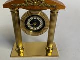 une petite horloge dorée avec un cadran noir, posée sur un socle