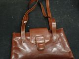 brown leather handbag with strap and buckles on a black surface