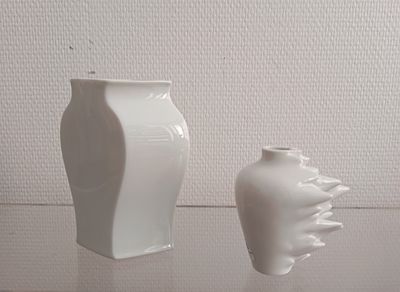 two white vases sitting on a table next to each other