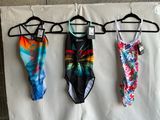 three swimsuits hanging on a clothes hanger on a wall