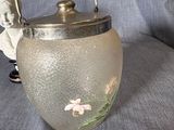 a glass tea pot with a silver handle on a blue cloth