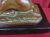 statue en bronze représentant un chien, posée sur un socle noir, elle-même posée sur une table rouge