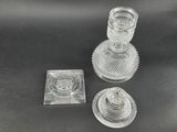 two clear glass candlesticks and a square glass coaster on a black surface