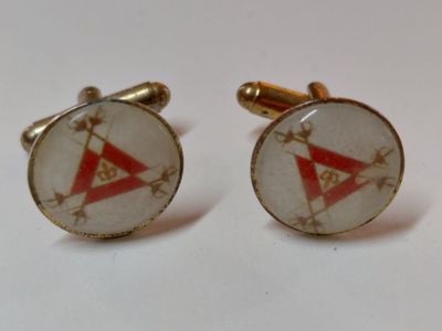 une paire de boutons de manchette ornés de symboles maçonniques sur un fond blanc