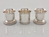 three silverplated cups are lined up on a white surface