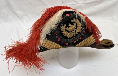 un chapeau noir orné de plumes rouges, posé sur une surface blanche