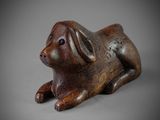 an old wooden figurine of a dog laying down on a gray surface