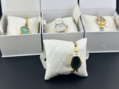 quatre montres dans une boîte posée sur une table noire, avec un coussin blanc