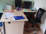 a desk with two computers and a chair in the corner