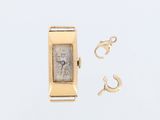 une montre en or et une paire de boucles d'oreilles posées sur une surface blanche