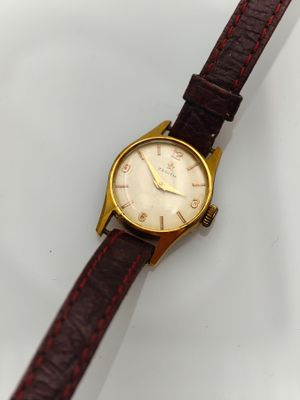 une photo d'une montre-bracelet posée sur une surface blanche, avec un bracelet rouge