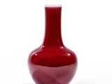 un vase rouge posé sur une surface blanche, avec un fond blanc