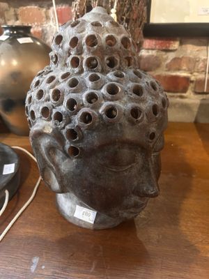 sculpture représentant une tête percée de trous, posée sur une table à côté d'une lampe