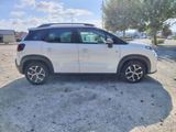 the white car is parked on the dirt in the parking lot