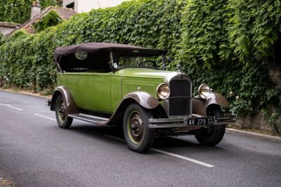 une voiture verte qui roule dans la rue devant un immeuble