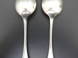 two silver spoons sitting on top of a table next to each other