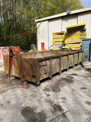 une benne à ordures placée devant un immeuble, à côté d'un tas de bois