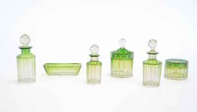 quatre flacons de parfum en verre vert et un bol en verre posés sur une surface blanche