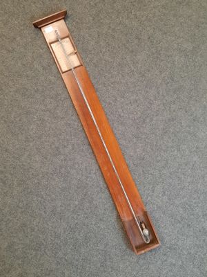 a long wooden clock with a metal handle on a carpeted floor