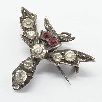 une broche ancienne en argent, ornée de pierres rouges et blanches sur un fond blanc