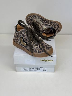 des chaussures de bébé à imprimé léopard posées sur une boîte, sur une surface blanche
