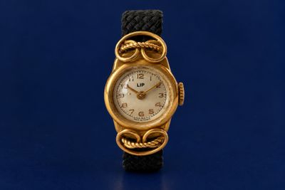 a gold wrist watch with a black band on a blue surface