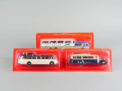 trois bus miniatures sont posés dans des boîtes en plastique sur une table