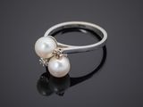 a white pearl and diamond ring on a black surface