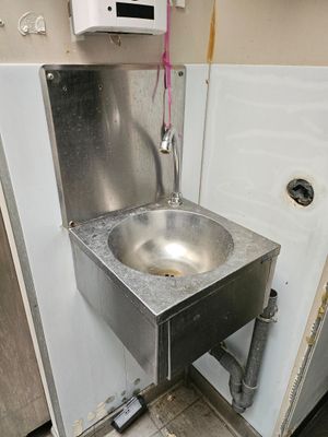 a metal sink in the corner of a public restroom