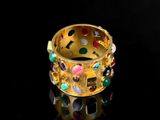 an image of a gold ring with multi colored stones on a black surface