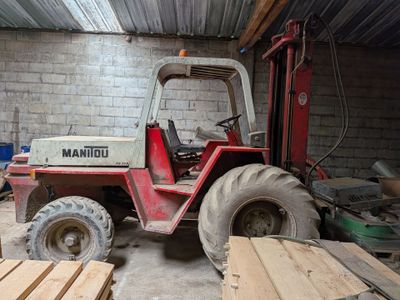 un chariot élévateur dans un garage, à côté d'un tas de bois