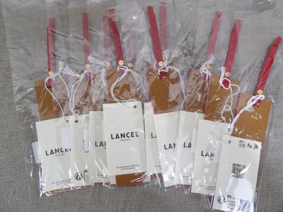 six bags of luggage tags are wrapped in plastic on a gray surface