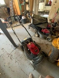 deux tondeuses à gazon dans un garage, avec un homme debout à côté d'elles