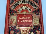 an old book with a red cover sitting on top of a table