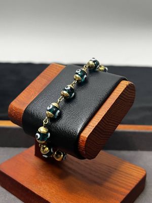 vitrine en bois sur laquelle est exposé un bracelet en perles noires et dorées