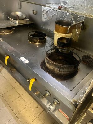 une cuisinière sale dans une cuisine professionnelle, avec des casseroles et des poêles posées dessus
