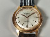 a gold wrist watch with a white dial on a black leather strap