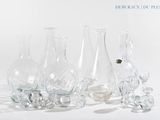 cinq vases en verre posés les uns à côté des autres sur une surface blanche
