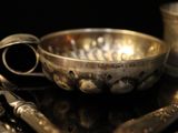 a silver bowl and spoon on a table with other silverware