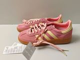 des baskets Adidas roses et jaunes posées sur une surface blanche, avec une étiquette de prix